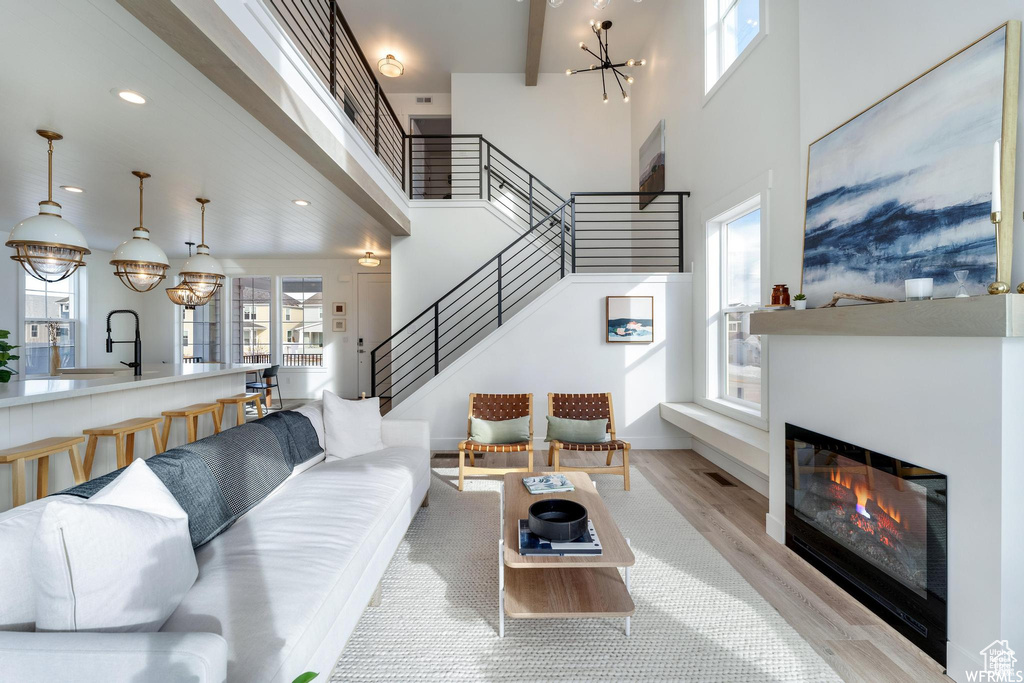 Living area with stairway, light wood-style flooring, a towering ceiling, a chandelier, and a glass covered fireplace