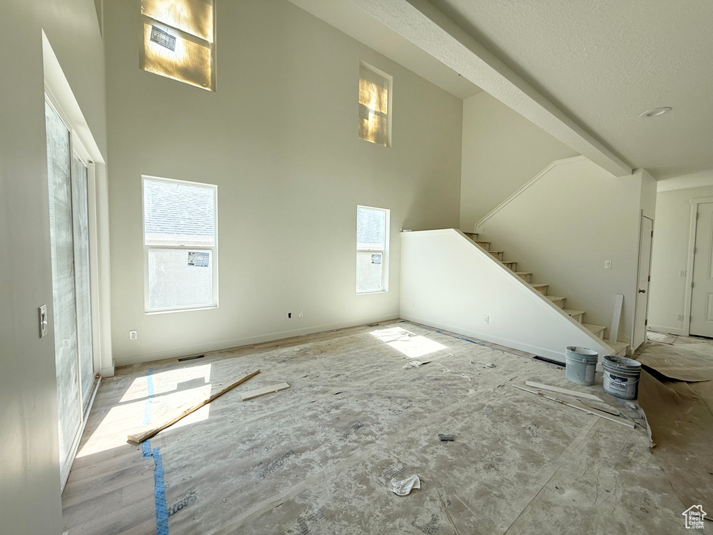 Unfurnished living room featuring plenty of natural light, stairway, and a high ceiling