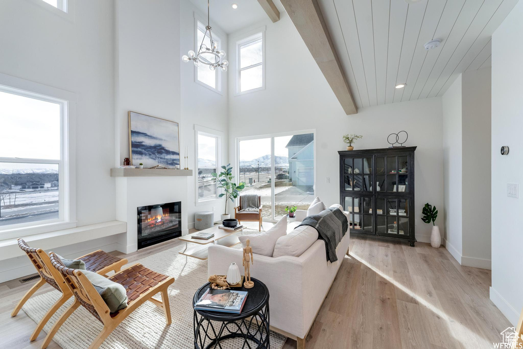 Living room with a glass covered fireplace, light wood finished floors, a high ceiling, baseboards, and a chandelier