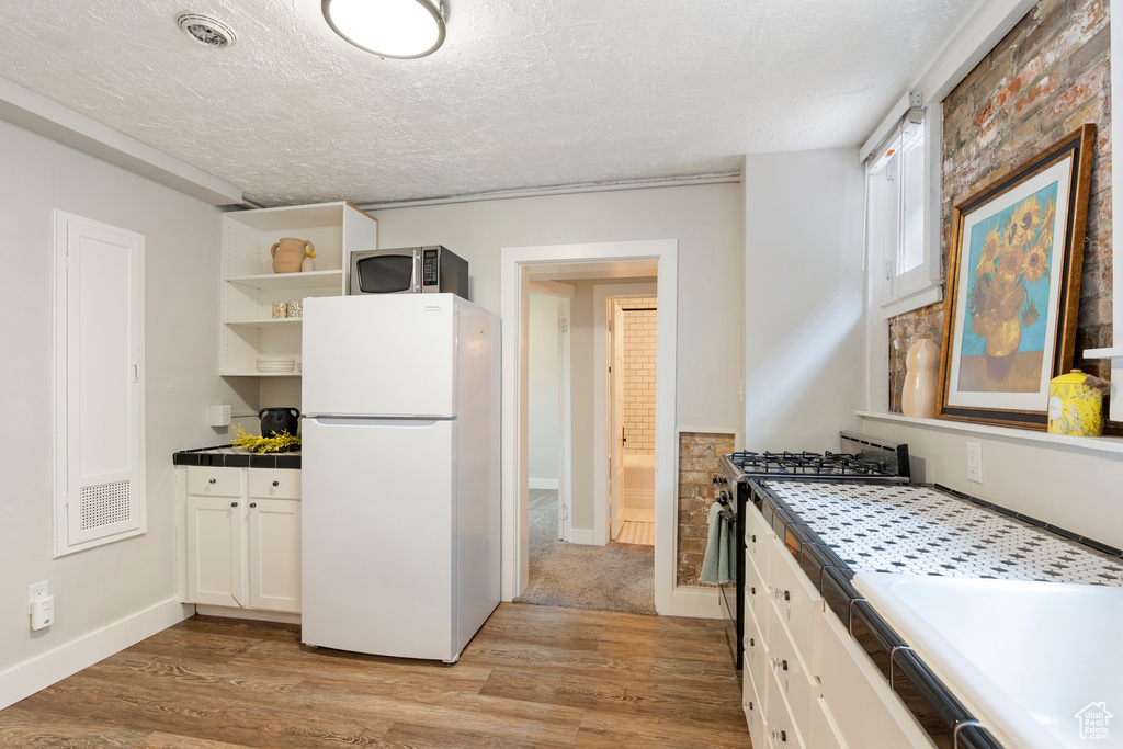 Kitchen with stainless steel appliances, tile countertops, light wood-style flooring, open shelves, and a textured ceiling