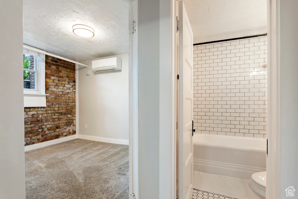 Full bath with an AC wall unit, a textured ceiling, toilet, baseboards, and  shower combination