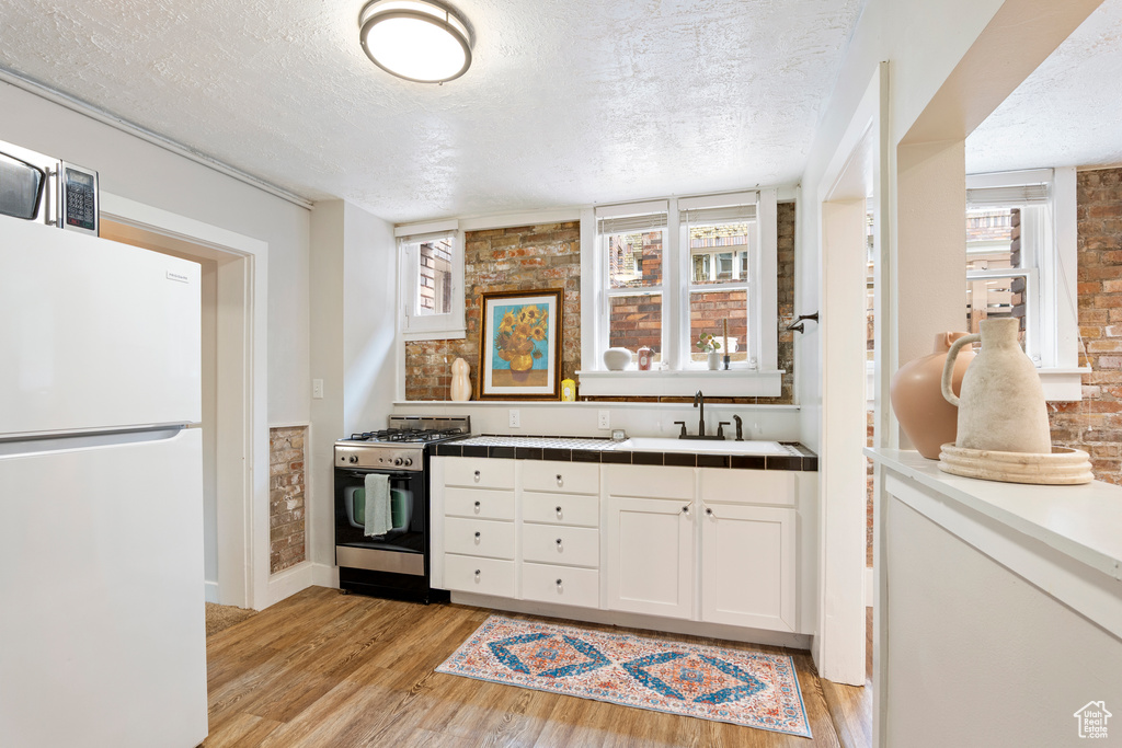 Kitchen with stainless steel gas stove, freestanding refrigerator, light wood-style flooring, a textured ceiling, and a sink