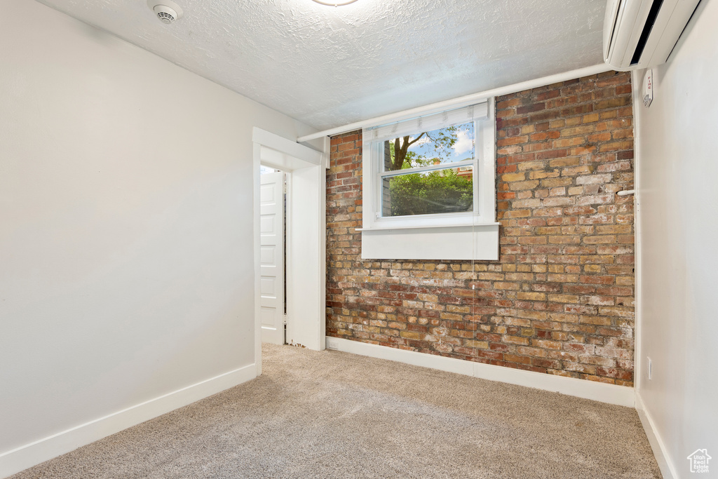 Spare room featuring an AC wall unit, carpet floors, a smoke detector, a textured ceiling, and baseboards