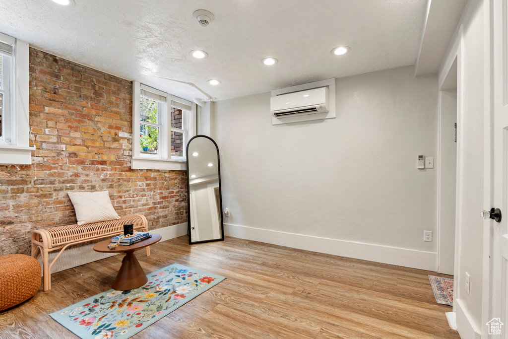 Sitting room featuring a wall mounted AC, baseboards, light wood finished floors, recessed lighting, and brick wall