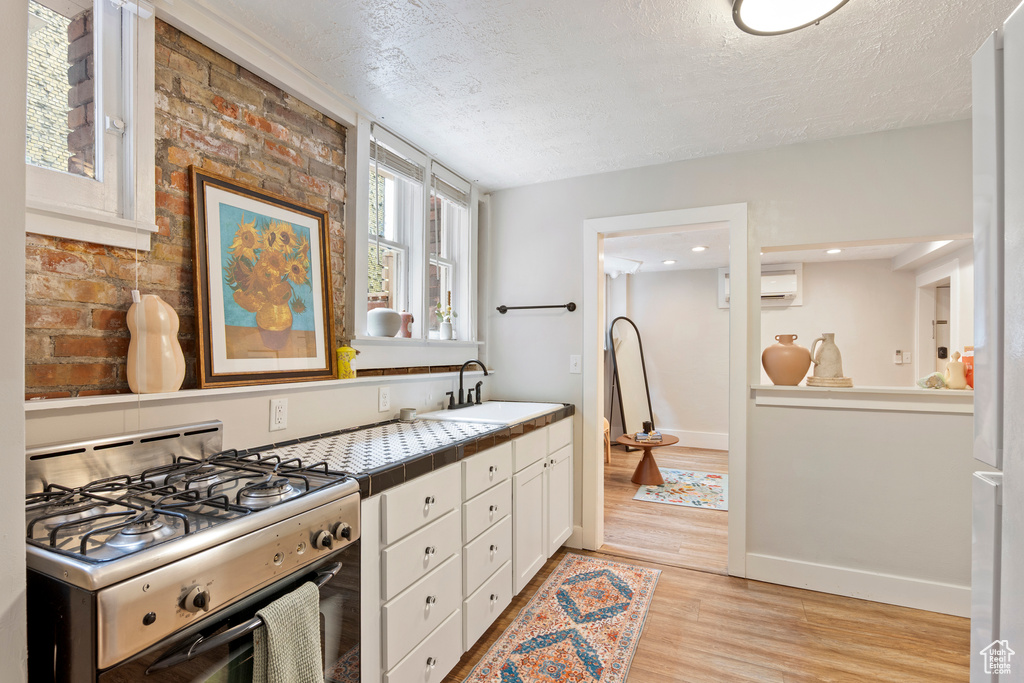 Kitchen with range with gas cooktop, a sink, a textured ceiling, tile countertops, and white cabinets
