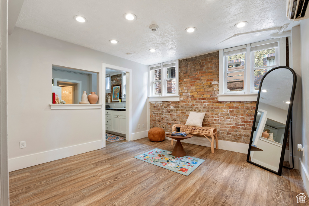 Living area with baseboards, light wood finished floors, recessed lighting, an AC wall unit, and brick wall