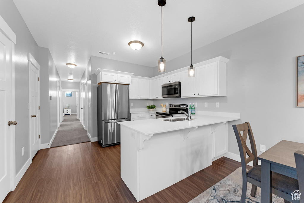 Kitchen with appliances with stainless steel finishes, a peninsula, light countertops, white cabinetry, and baseboards