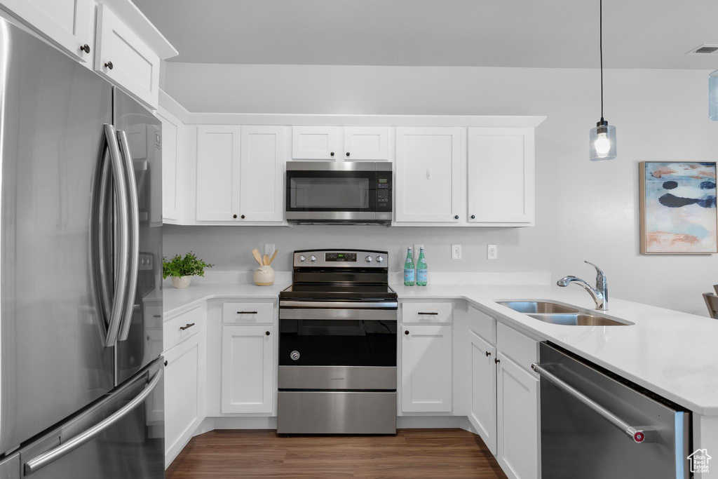 Kitchen featuring stainless steel appliances, a sink, a peninsula, dark wood finished floors, and white cabinetry