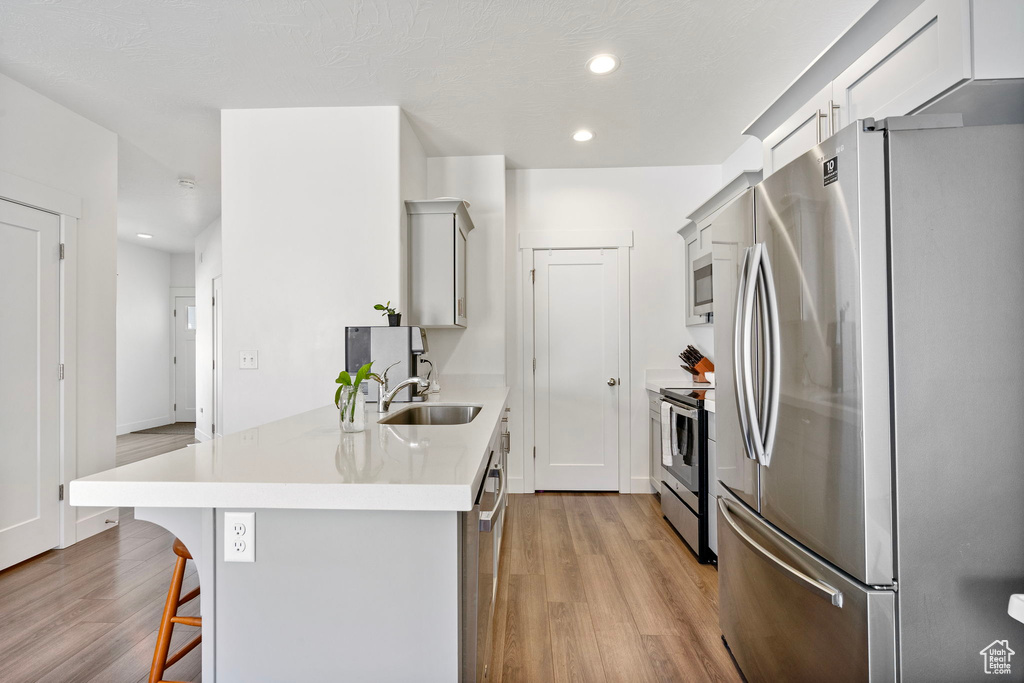 Kitchen featuring appliances with stainless steel finishes, a kitchen bar, light wood-style floors, light countertops, and recessed lighting