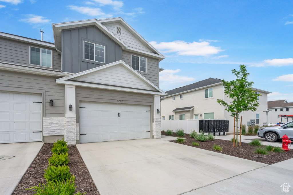 View of front of property with board and batten siding, stone siding, a garage, and driveway