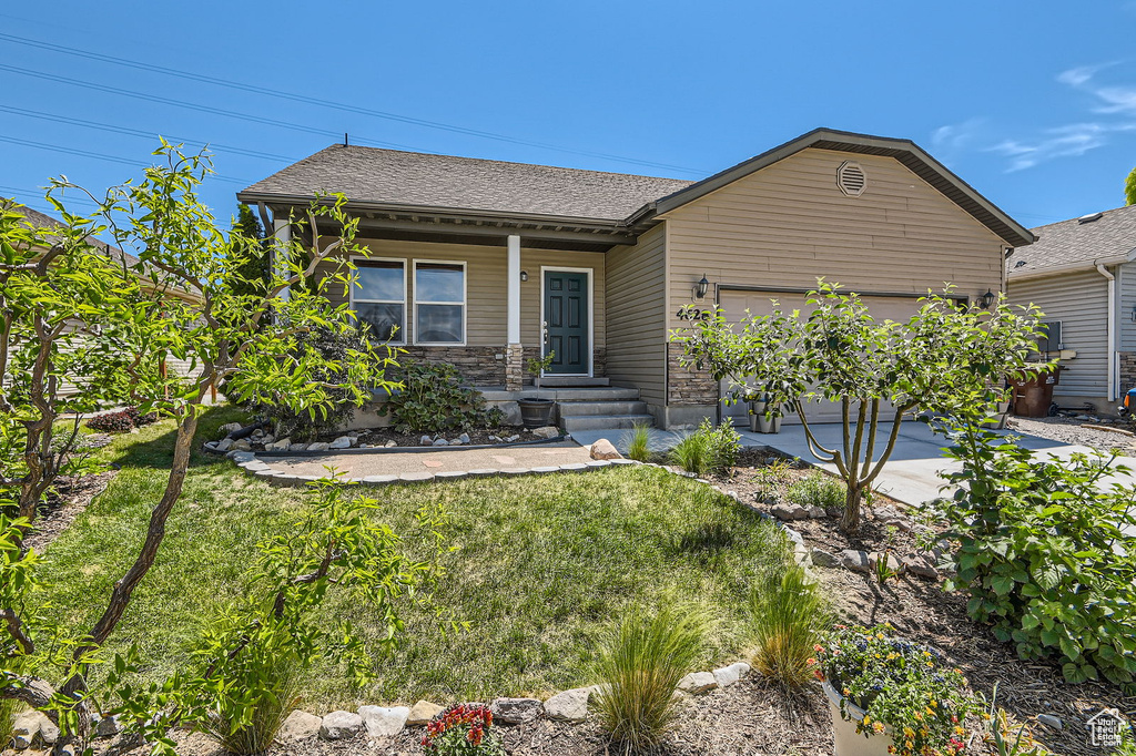 View of front facade featuring a garage, a front yard, driveway, covered porch, and roof with shingles