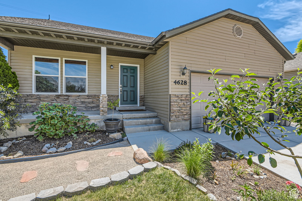 View of front facade featuring an attached garage, covered porch, stone siding, and driveway