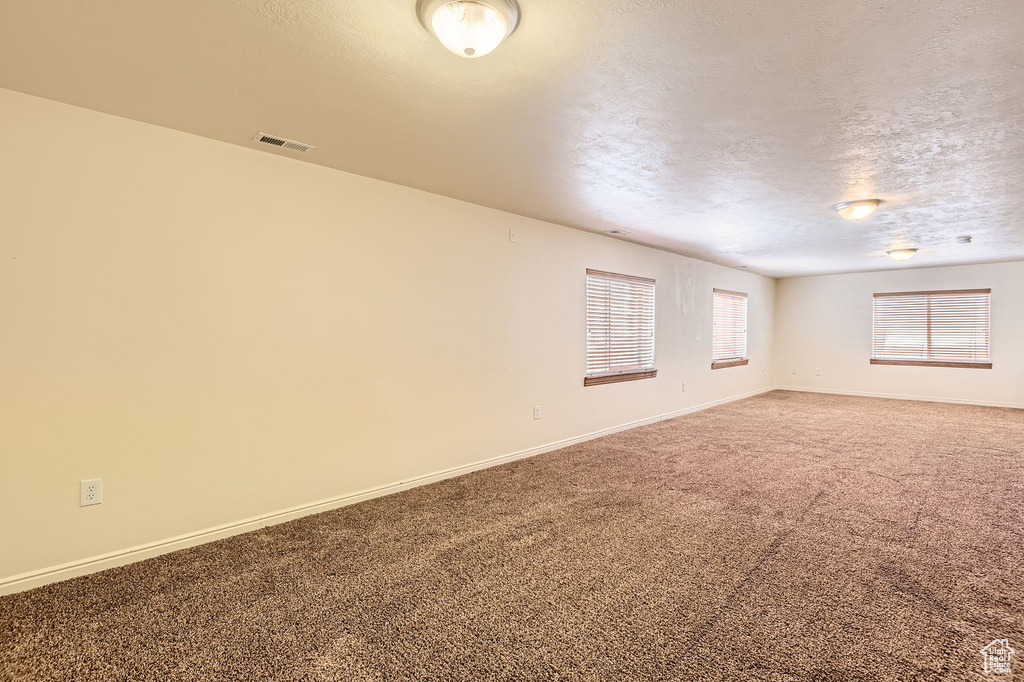 Carpeted spare room featuring baseboards and a textured ceiling