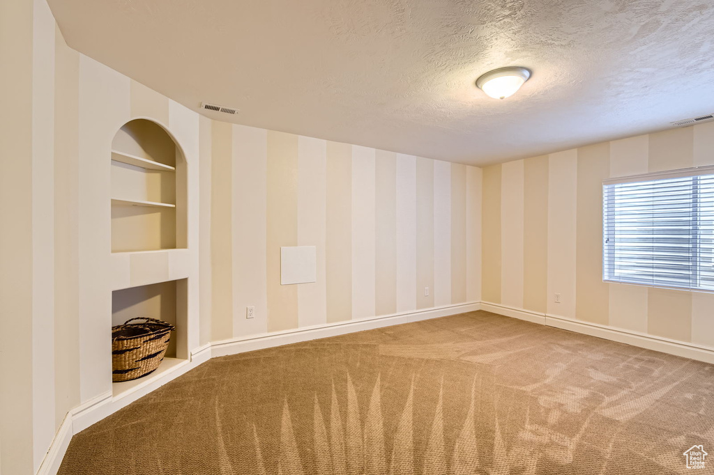 Carpeted empty room with baseboards, a textured ceiling, and built in shelves