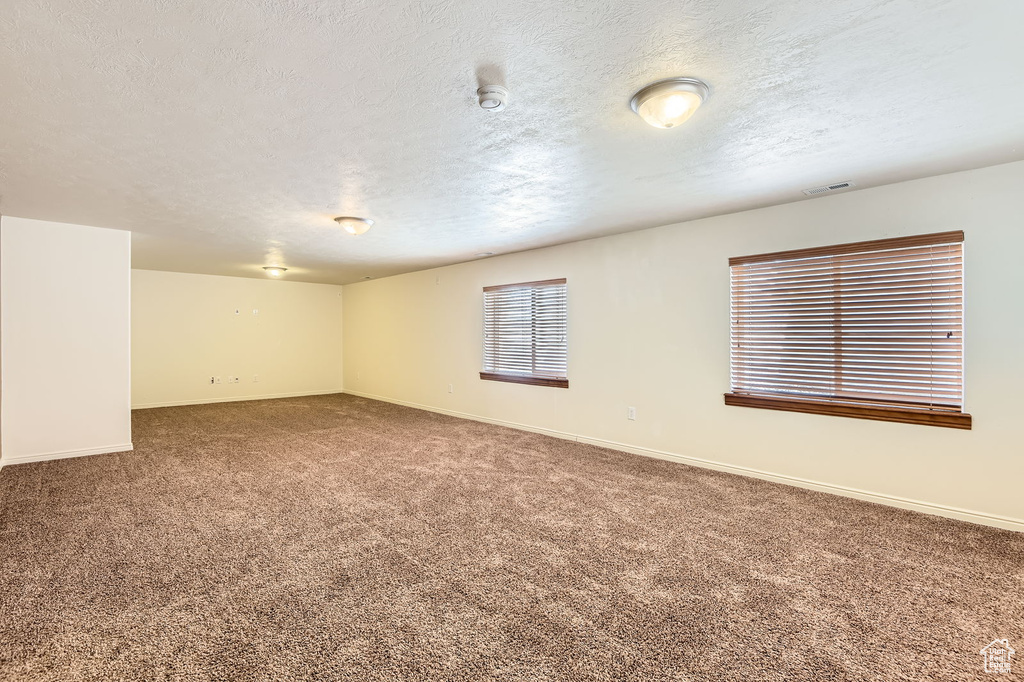 Carpeted spare room featuring a textured ceiling, baseboards, and a smoke detector