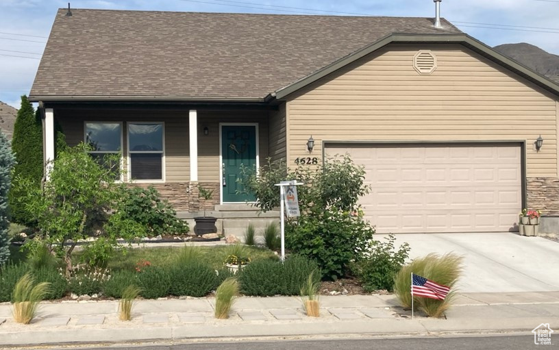 View of front of property with concrete driveway, an attached garage, a shingled roof, and stone siding