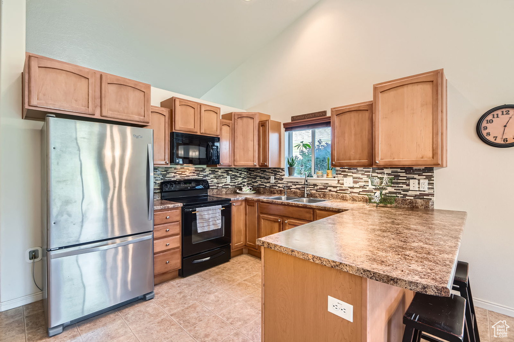 Kitchen featuring black appliances, a peninsula, a sink, tasteful backsplash, and high vaulted ceiling