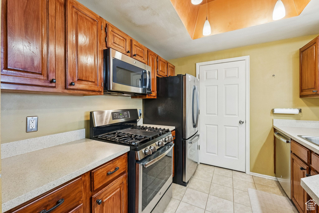 Kitchen with stainless steel appliances, light countertops, light tile patterned floors, and brown cabinetry