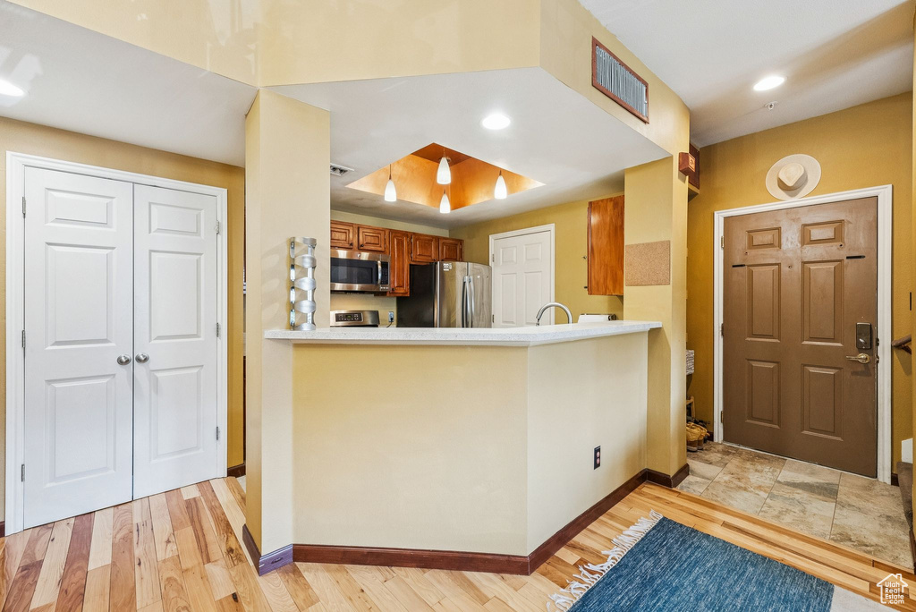 Kitchen with stainless steel appliances, brown cabinets, baseboards, light wood-style flooring, and a peninsula