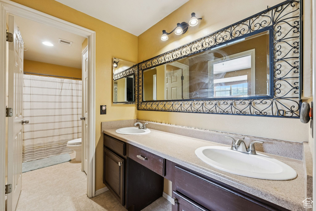 Bathroom with toilet, double vanity, a shower with curtain, and baseboards