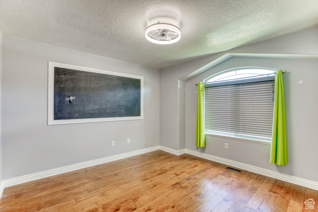 Empty room featuring hardwood / wood-style floors, a textured ceiling, baseboards, and vaulted ceiling