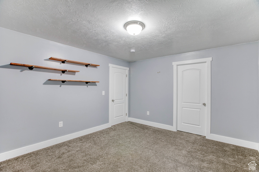 Carpeted empty room featuring a textured ceiling and baseboards