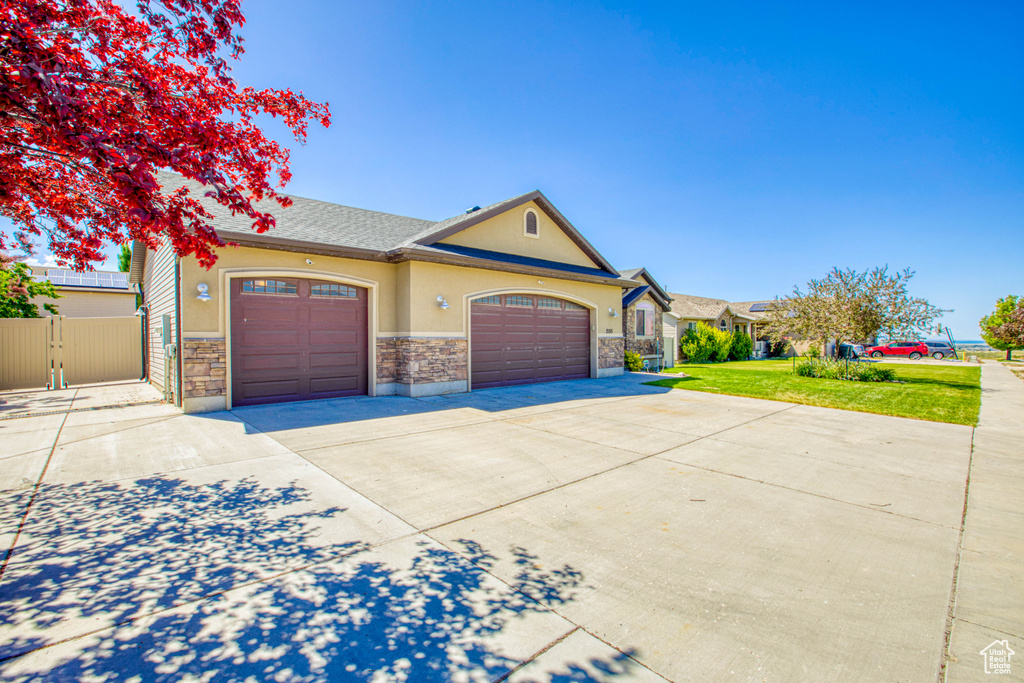 View of front of property with stucco siding, concrete driveway, an attached garage, stone siding, and a gate