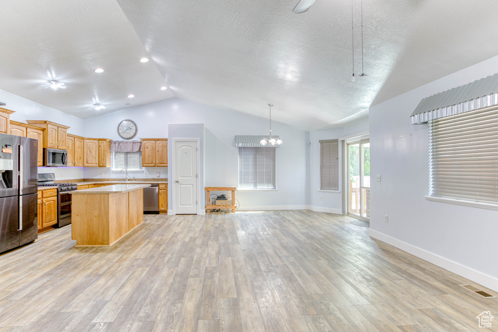 Kitchen featuring appliances with stainless steel finishes, vaulted ceiling, light countertops, a kitchen island, and open floor plan