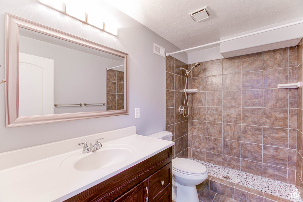 Full bathroom featuring toilet, vanity, a tile shower, and a textured ceiling