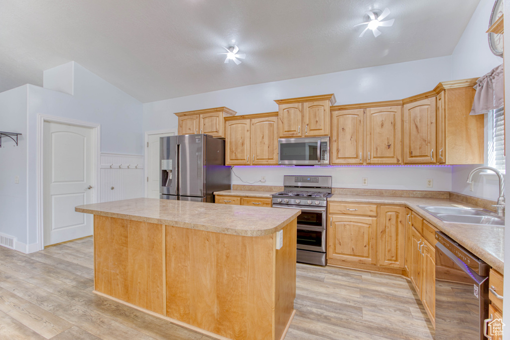 Kitchen featuring stainless steel appliances, a sink, light countertops, a center island, and light wood-style floors