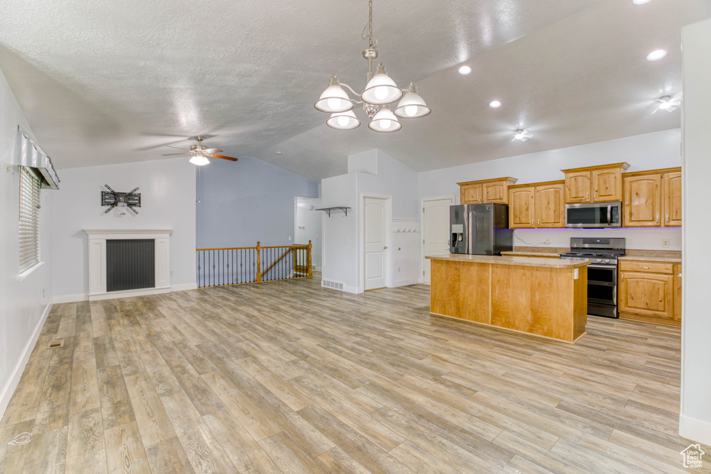 Kitchen featuring appliances with stainless steel finishes, open floor plan, a center island, lofted ceiling, and a ceiling fan