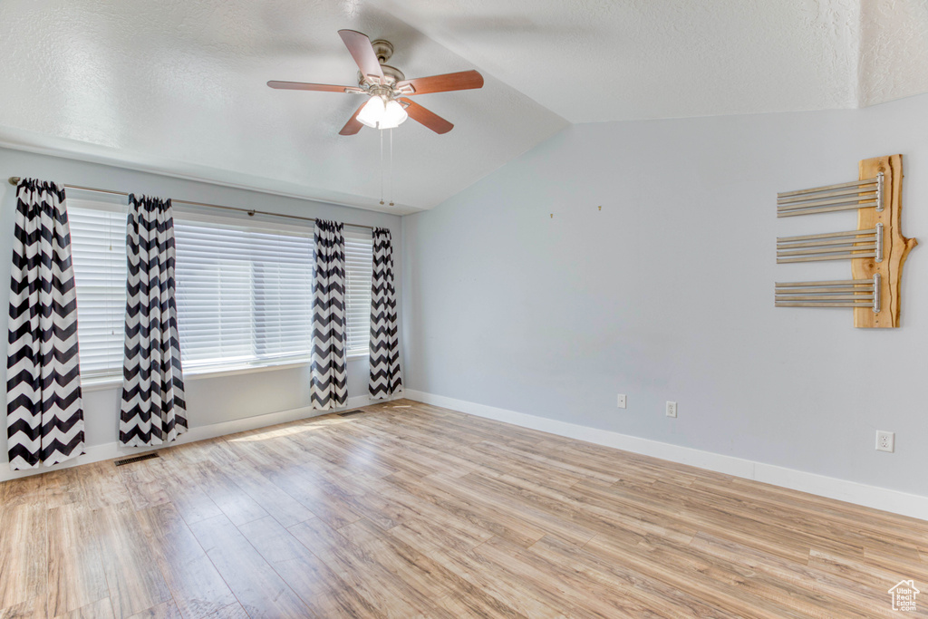 Empty room with wood finished floors, ceiling fan, vaulted ceiling, radiator, and baseboards