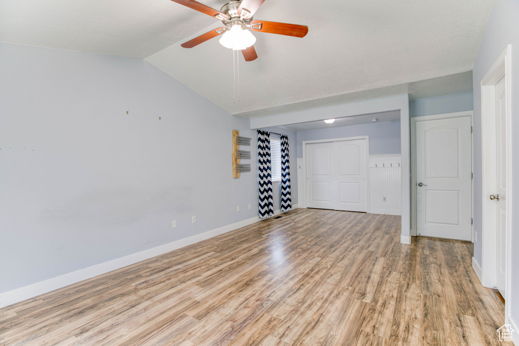Empty room with light wood finished floors, a ceiling fan, vaulted ceiling, and baseboards