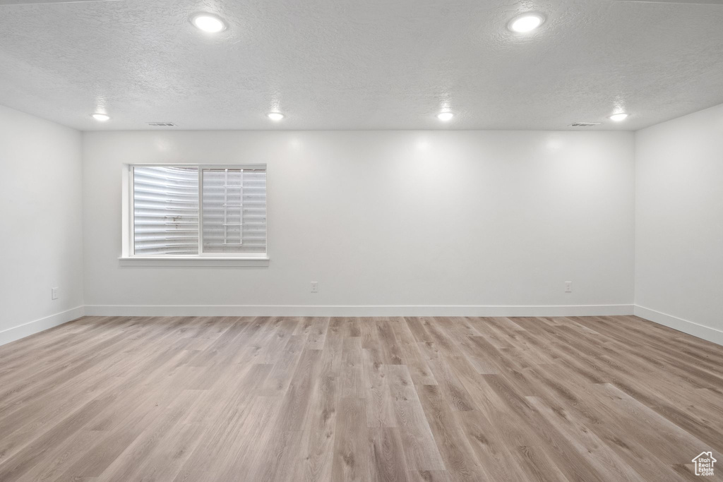 Empty room featuring a textured ceiling, light wood-type flooring, recessed lighting, and baseboards