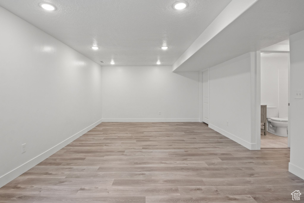 Finished below grade area with recessed lighting, light wood-type flooring, baseboards, and a textured ceiling