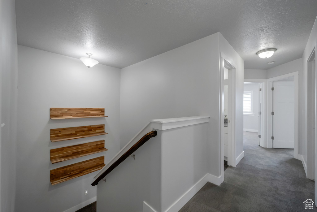 Hall featuring an upstairs landing, a textured ceiling, baseboards, and carpet flooring