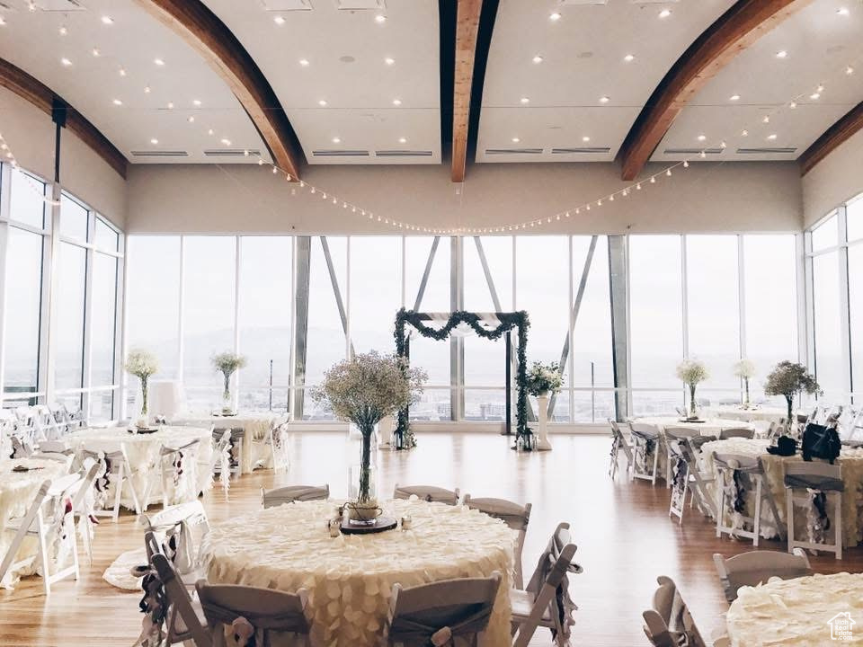 Dining room featuring beam ceiling, wood finished floors, a wall of windows, a high ceiling, and plenty of natural light