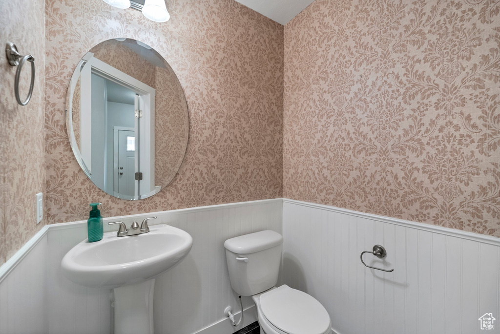 Half bathroom featuring wallpapered walls, a wainscoted wall, and toilet