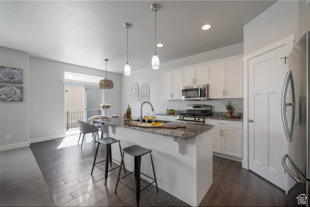 Kitchen featuring appliances with stainless steel finishes, a sink, dark wood-type flooring, dark stone counters, and recessed lighting