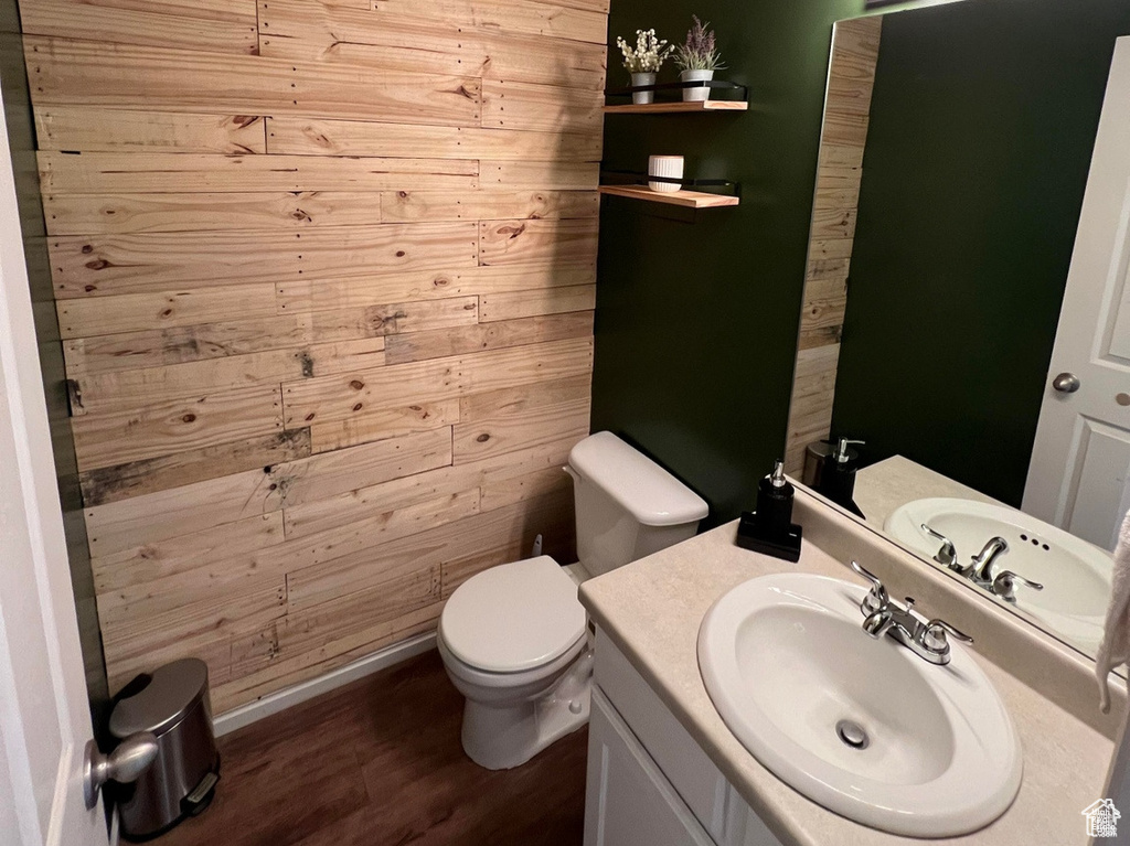 Bathroom with wood finished floors, vanity, toilet, wooden walls, and baseboards