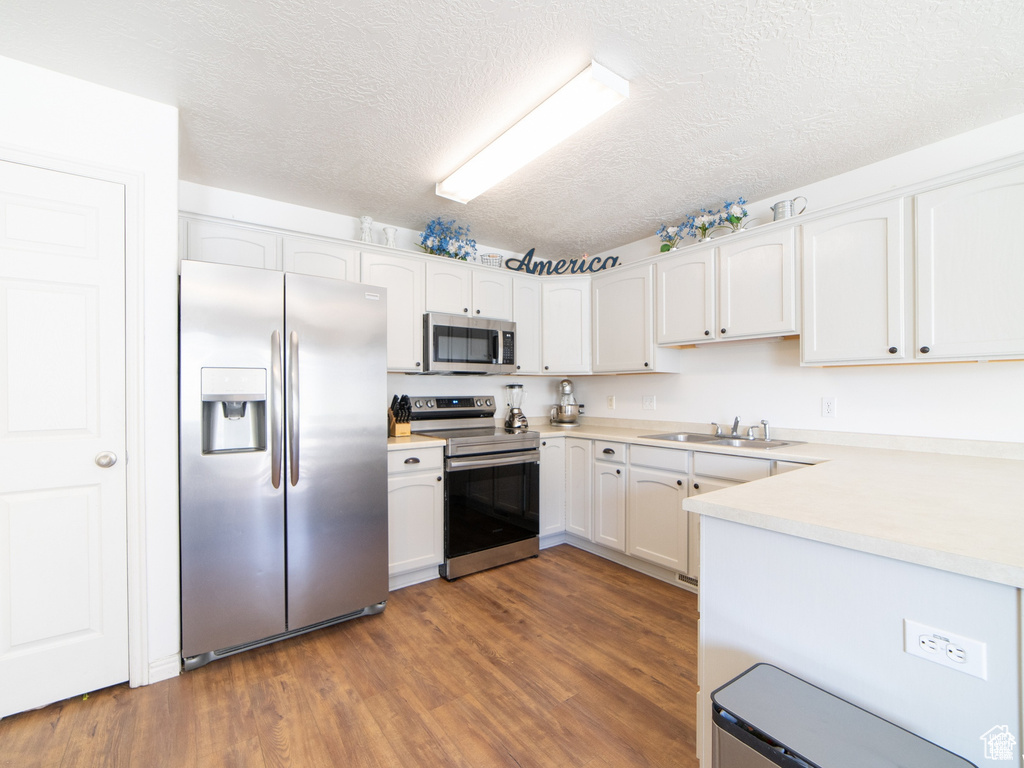 Kitchen with appliances with stainless steel finishes, a sink, dark wood-type flooring, white cabinets, and light countertops