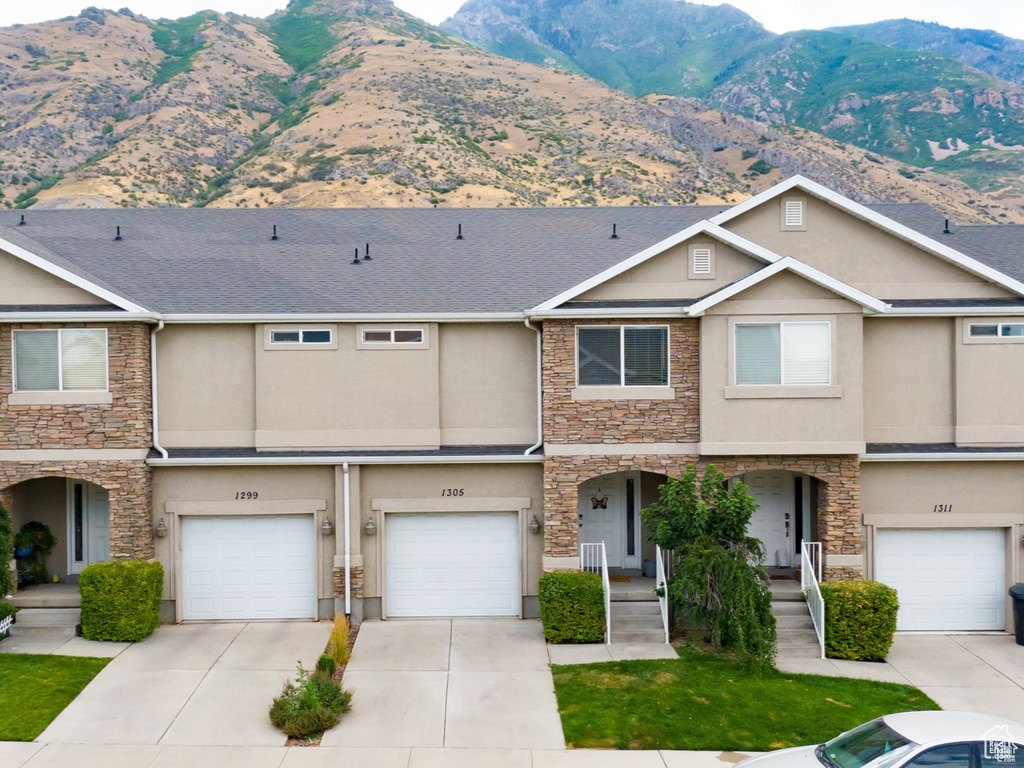 Townhome / multi-family property with stone siding, stucco siding, a mountain view, a garage, and driveway