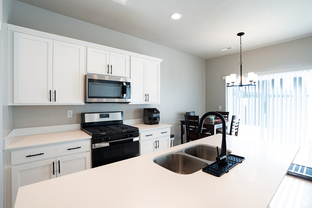 Kitchen featuring stainless steel appliances, light countertops, recessed lighting, white cabinets, and hanging light fixtures