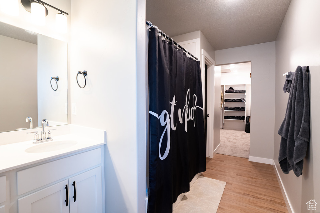 Full bath with vanity, wood finished floors, a shower with curtain, a spacious closet, and baseboards