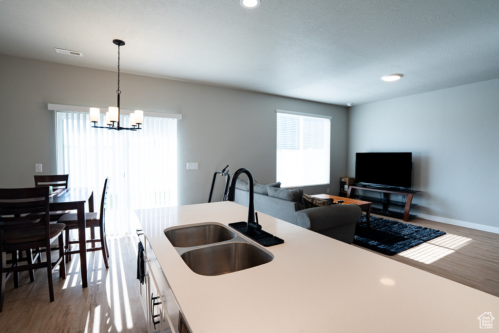 Kitchen with a sink, wood finished floors, a chandelier, light countertops, and recessed lighting