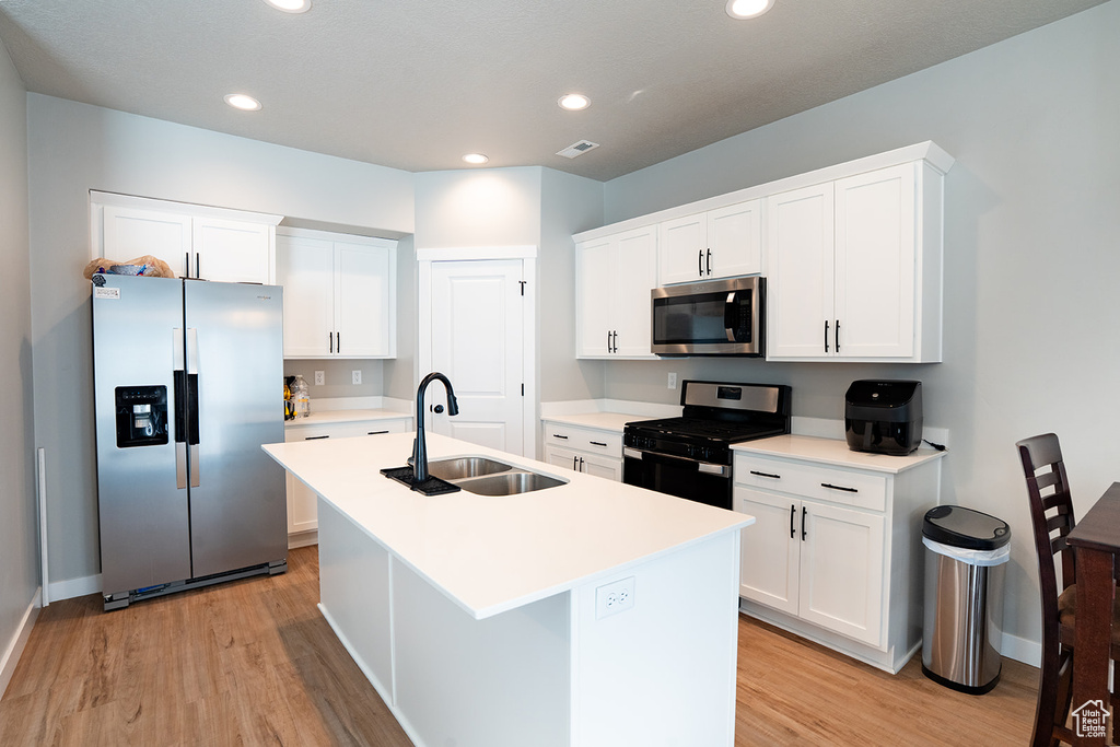 Kitchen with appliances with stainless steel finishes, a sink, light wood-style flooring, a kitchen island with sink, and white cabinets