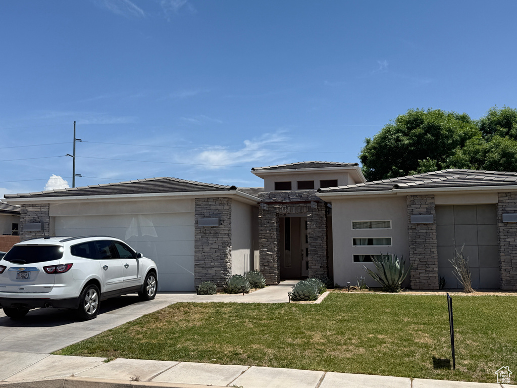 Prairie-style home with a garage, driveway, stone siding, and a front yard