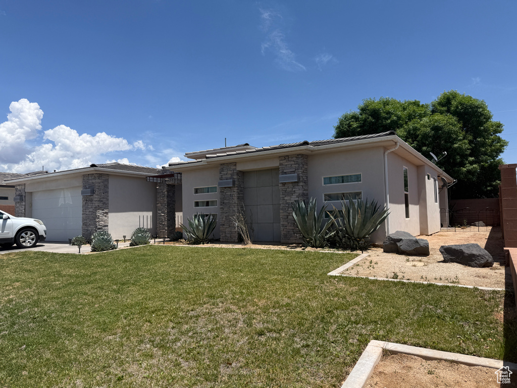 View of front of property with an attached garage, stucco siding, stone siding, and a front yard