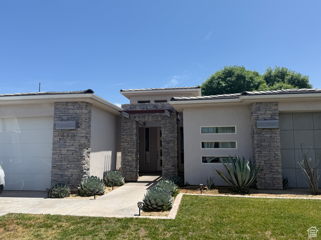 View of front of house with stucco siding, stone siding, a front yard, and a garage