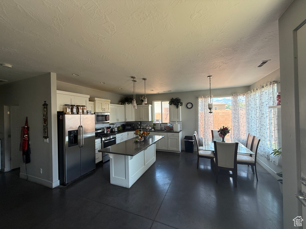 Kitchen with stainless steel appliances, a textured ceiling, dark countertops, white cabinets, and a kitchen island